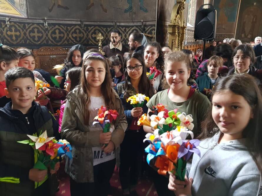Copii zâmbitori cu flori din hârtie în mâini, în biserică
