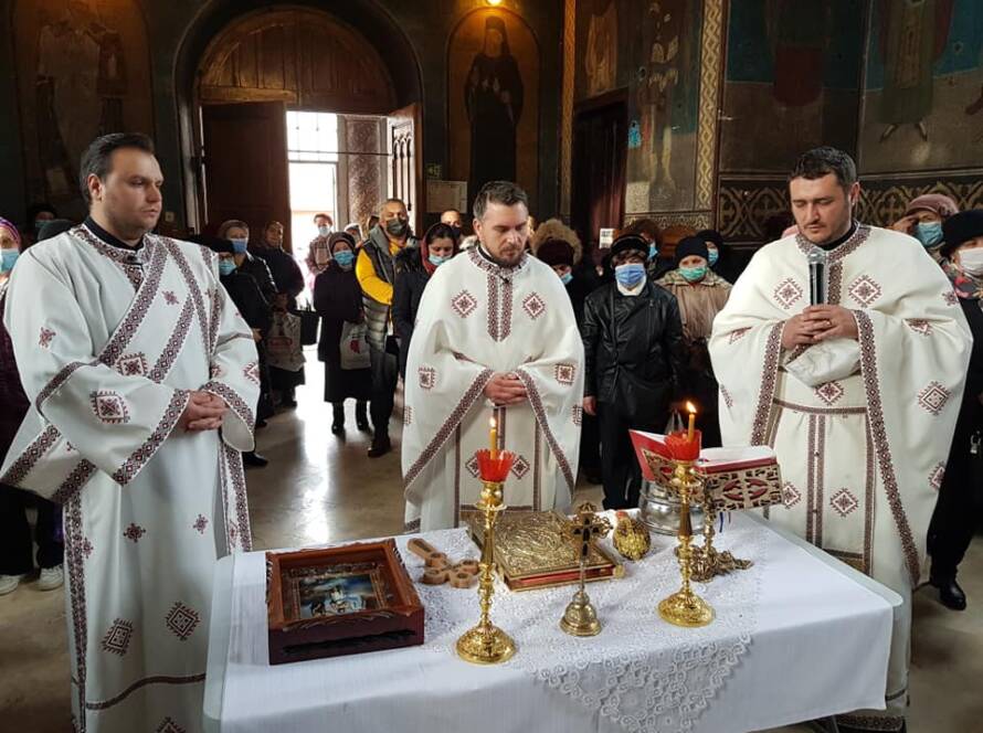 Trei slujitori în veșminte albe, în rugăciune lângă masa pregătită pentru sfințirea Aghesmei Mari
