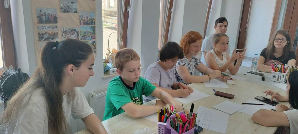 Copii la masa de lucru, cu creioane colorate, în timpul unui atelier