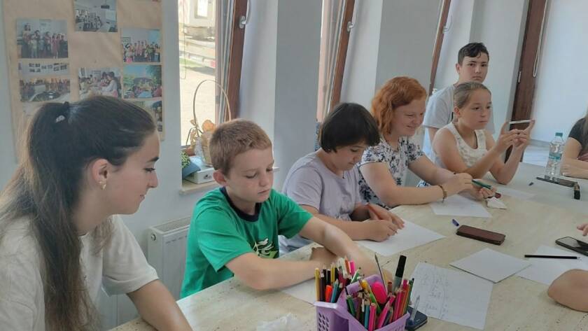 Copii la masa de lucru, cu creioane colorate, în timpul unui atelier