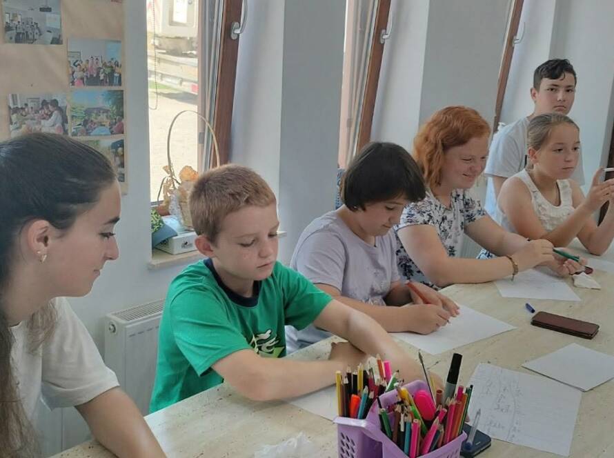 Copii la masa de lucru, cu creioane colorate, în timpul unui atelier