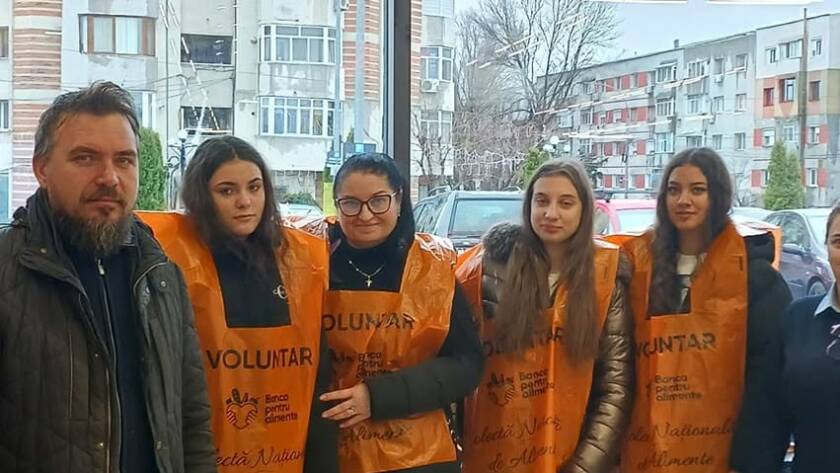 Un grup de voluntari în veste portocalii, împreună cu un bărbat, la intrarea în magazin