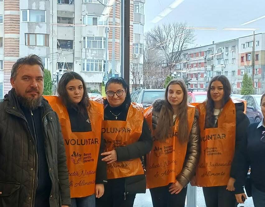 Un grup de voluntari în veste portocalii, împreună cu un bărbat, la intrarea în magazin