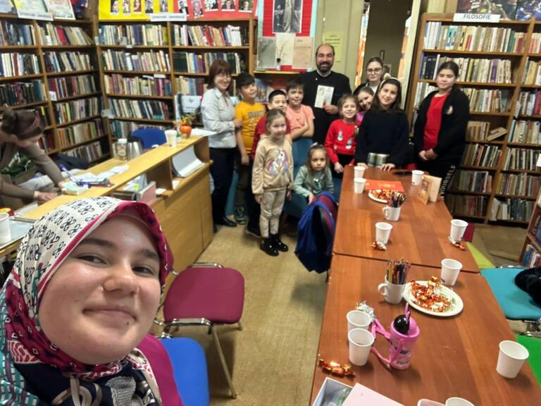 Fotografie de grup cu copiii, preotul și voluntarele, între rafturile bibliotecii