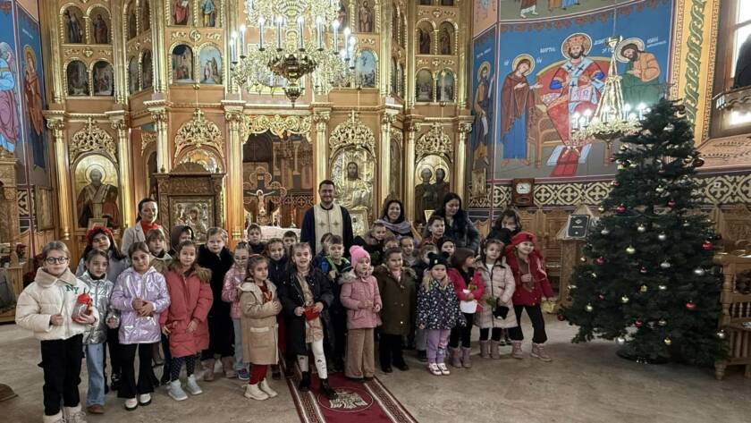Elevii claselor pregătitoare și I, alături de un preot și de mai mulți adulți, în Catedrala „Sfinții Apostoli Petru și Pavel”, lângă bradul de Crăciun