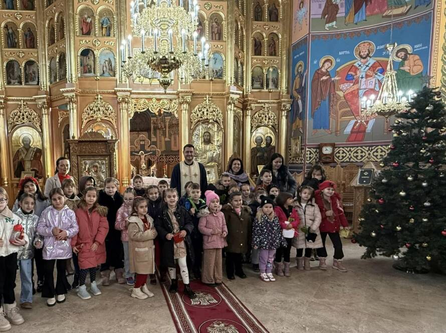 Elevii claselor pregătitoare și I, alături de un preot și de mai mulți adulți, în Catedrala „Sfinții Apostoli Petru și Pavel”, lângă bradul de Crăciun