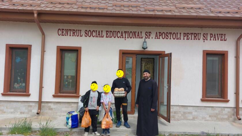Copii și adulți alături de un preot, cu alimente în fața centrului social-educațional