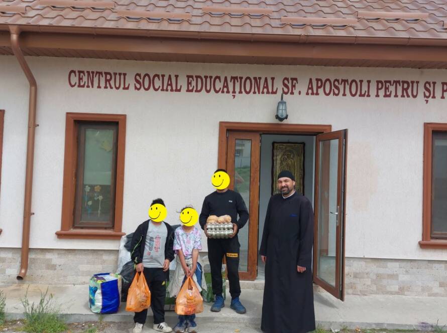 Copii și adulți alături de un preot, cu alimente în fața centrului social-educațional