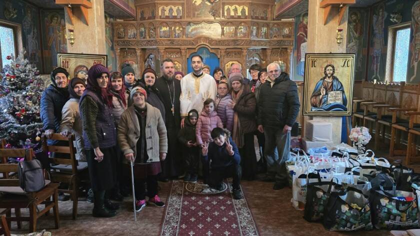 Grup de credincioși și preoți în biserică, în jurul darurilor pregătite, lângă bradul de Crăciun
