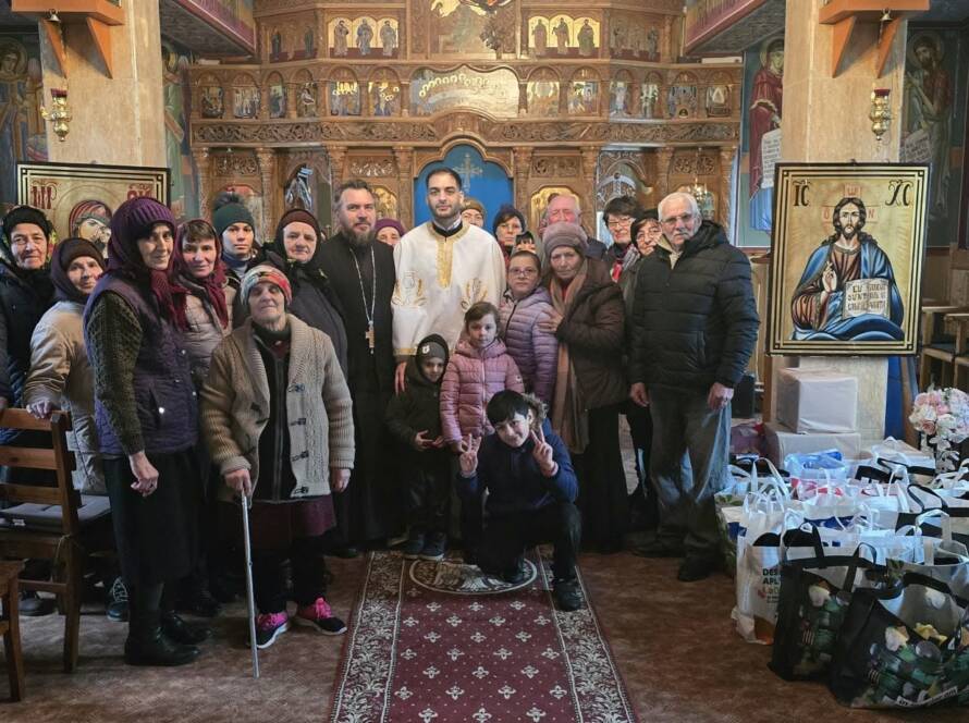 Grup de credincioși și preoți în biserică, în jurul darurilor pregătite, lângă bradul de Crăciun