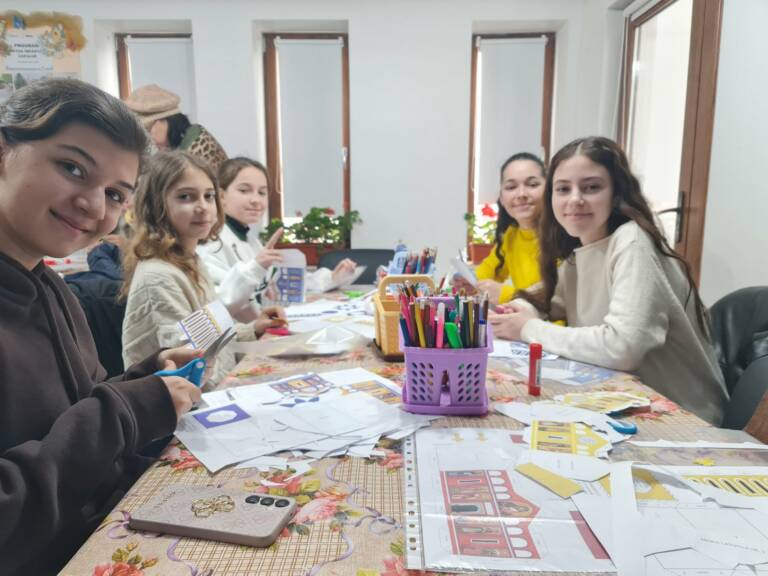 Copii zâmbind la masa de lucru, printre piesele machetelor și creioanele colorate