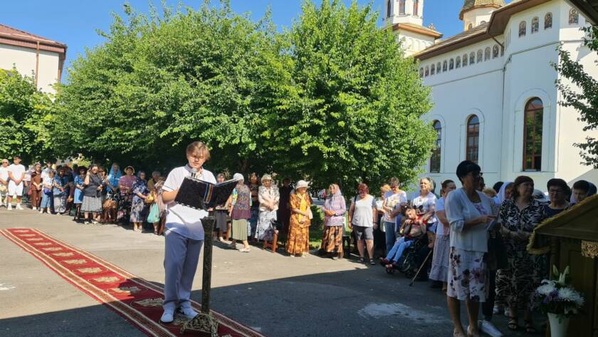 Un tânăr citește la strană în fața credincioșilor, în curtea bisericii, la sărbătoarea hramului.
