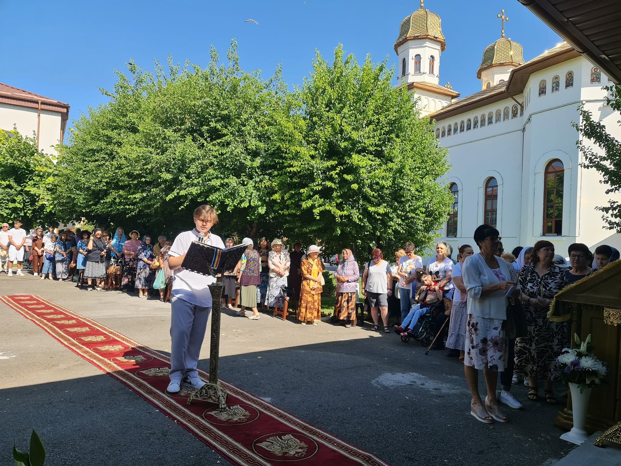 Un tânăr citește la strană în fața credincioșilor, în curtea bisericii, la sărbătoarea hramului.