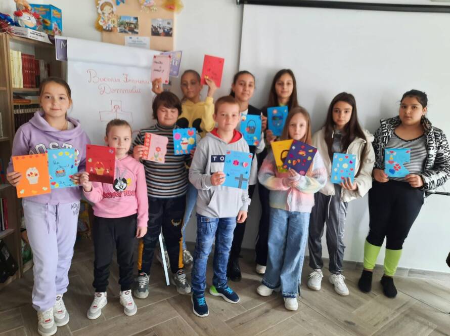 Grup de copii arătând felicitările de Paști realizate la atelier, în sala parohială