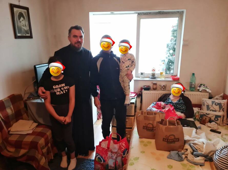Un preot alături de o familie și mai multe pachete cu alimente
